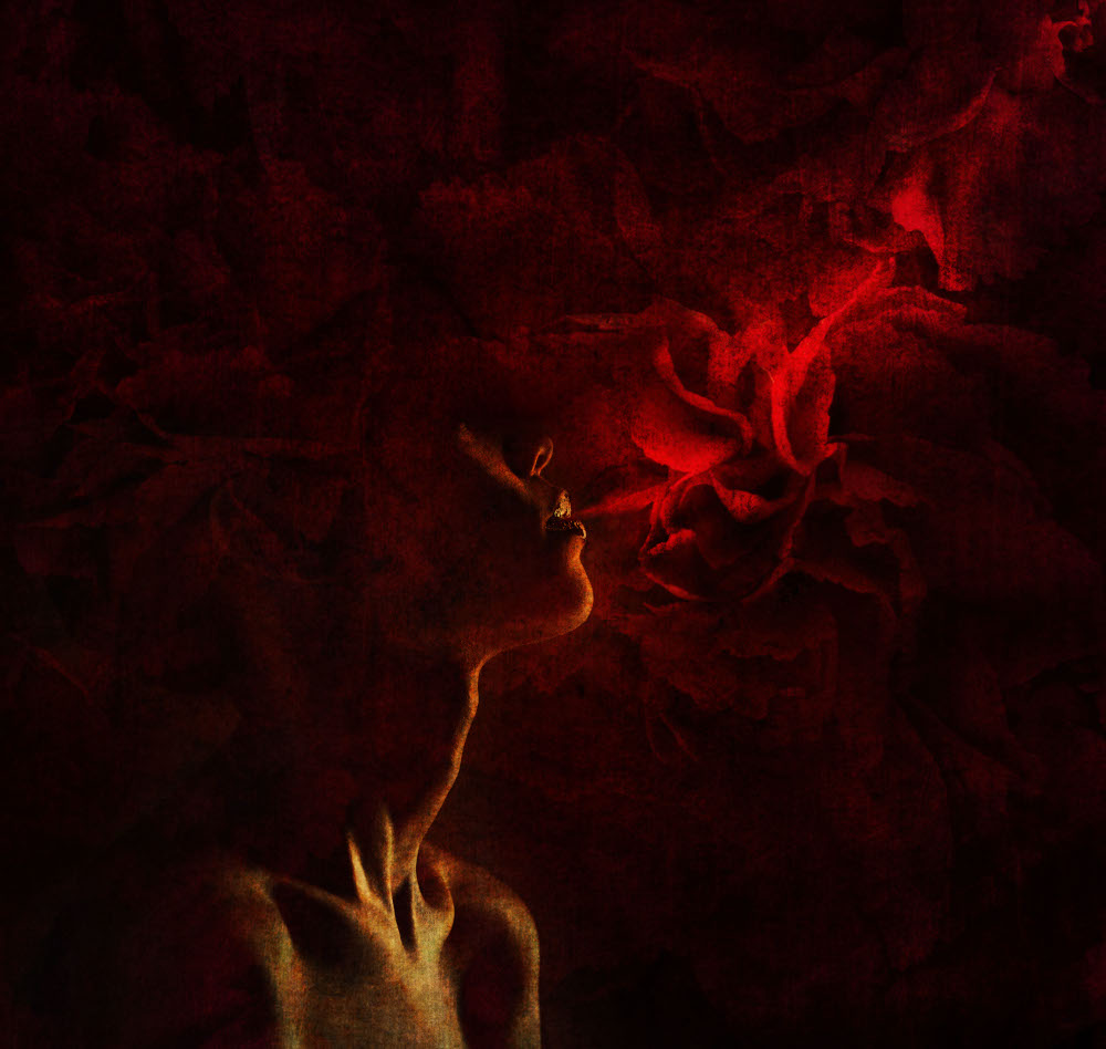 A woman with red roses woven into her hair, her breath illuminated against a blurred natural background.